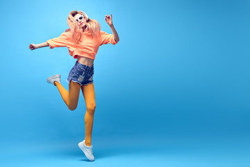 Obraz premium Fashion Hipster DJ Girl in trendy colorful neon Outfit Fooling Around dance. Young shapely blond Woman listen to music Having Fun relax. Art neon fashionable style. Funny happy positive concept