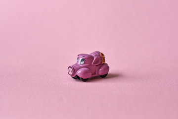 Pink toy car delivering products on a pink background. Postcard February 14, Valentine's Day. Flower delivery.