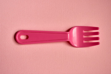 Close-up of one childish plastic pink forks on a pale pink background. Dishes for a picnic.
