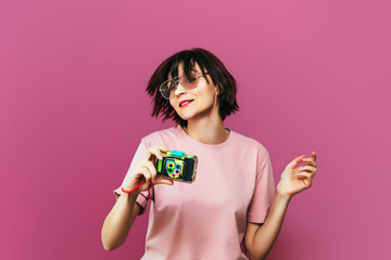 Young pretty girl in sunglasses with hipster camera. Colored background. Pink