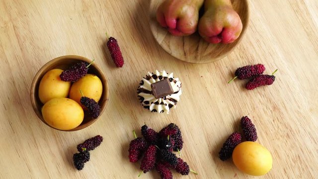 Top view of delicious cupcake and different kinds of fruit on a wooden board