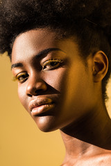 beautiful african american woman with yellow eyelashes looking at camera isolated on brown