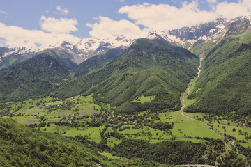 Fototapeta na wymiar Scenic valley in the Caucasus Mountains with a small village, summer greens and snow-capped peaks