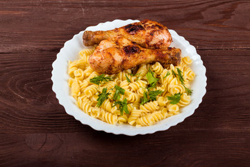 Grilled chicken drumstick and pasta on white plate, brown wooden background