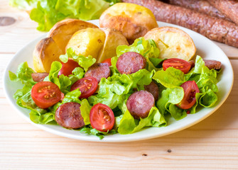 Smoked sausage with vegetables salad on a wooden board
