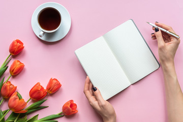 Obraz premium Notebook with cup of tea and beautiful red tulips on pink background. Place for your texy