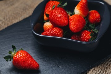 Washed strawberries in sieve on stone background. Close up of washed strawberries in sieve with three fresh and juicy strawberries near it on stone background