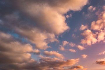 Blue sky background with evening fluffy curly rolling altocumulus altostratus clouds with setting sun. Good windy weather