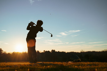 Fototapeta na wymiar Young junior golfer practicing in a driving range with beautiful sunset light in winter.