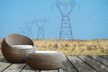 A set of round wicker chair on old wooden deck with view of high voltage power towers in field with blue sky.