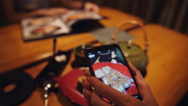 A woman takes a photograph dessert on a smartphone in a Japanese restaurant.