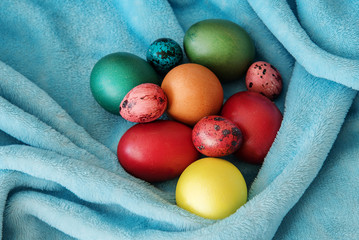 many colored Easter eggs of different sizes on a blue soft blanket