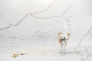 Closeup of a marble looking quartz countertop with beautiful natural stone veining, decorated by a glass jar of sea shells