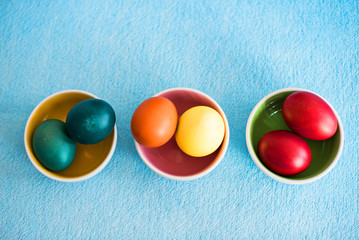 cute Easter colored eggs of different sizes in small bowls on blue background