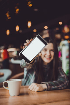 blurry portrait of a happy smiling brunette girl who holds a mobile phone with a clean screen ready for your logo or text..