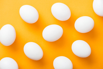top view of whole white fresh chicken eggs on bright orange background