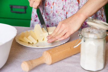 Woman standing by the wooden table in the kitchen and cutting butter into apple pie