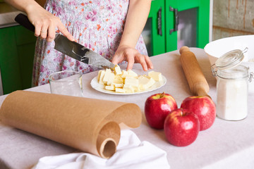 Woman cutting butter on white plate for homemade pie on white tabletop with apples, rolling pin and a bowl of flour