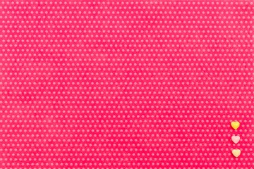 Yellow and pink small hearts in a corner vertically on a textile background, fuchsia with a print in white polka dots. View from above.