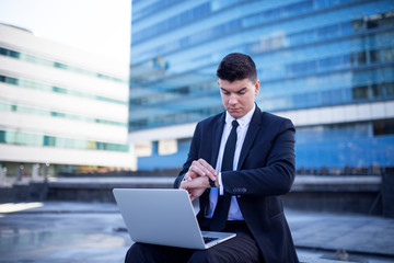 Fototapeta premium Confident young businessman using laptop in a front of building