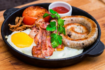 Nutritious meal with fried egg, sausage, bacon, tomato and sauce in frying pan