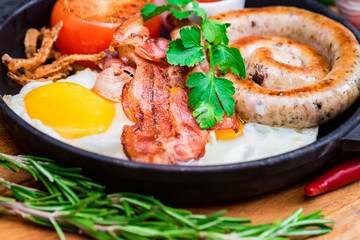 Nutritious meal with fried egg, sausage, bacon, tomato and sauce in frying pan