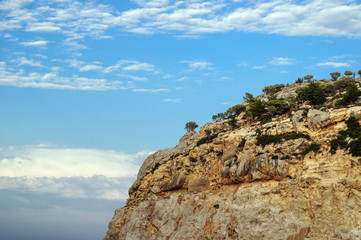 Steep rock with trees against a blue sky.