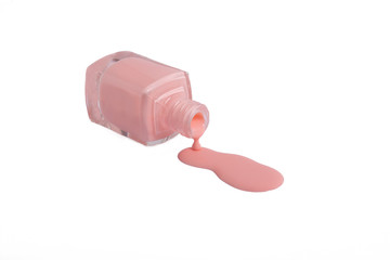 Pink nail polish is poured from the bottle on the table on a white background