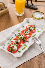 Tomato salad with basil, cheese, olive oil and glass of juice on wooden table