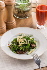 Spicy Beef Salad with green mix and tomato juice on wooden table