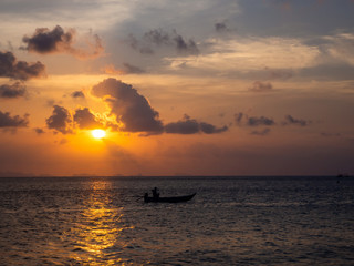 Silhouettes of people in a kayak in the rays of the setting sun against the background of clouds. Ko Phangan.Thailand.