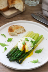 Breakfast consisting of poached egg and boiled asparagus with butter and lettuce on a wooden surface. Rustic style.