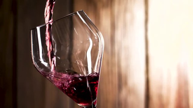 Wein. Rotwein, der in Weinglas &uuml;ber dunklem Hintergrund gie&szlig;t.