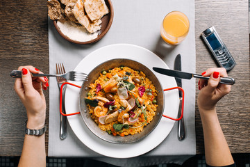 Woman eating tasty paella with seafood in restaurant
