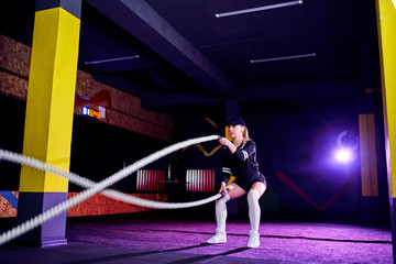 Fitness woman using training ropes for exercise at gym. Athlete working out with battle ropes at cross gym.