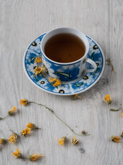 A cup of warm herbal tea from a medicinal calendula and orange marigold flowers on a gray wooden table. Top view. Copy space