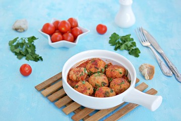 Fish meatballs in tomato sauce in a white ceramic pan on a light blue concrete background