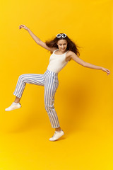 Fototapeta na wymiar Vertical portrait of energetic active young woman wearing stylish trendy clothes fooling around, moving body as if dancing, smiling happily. People, youth, lifestyle, joy, fun and happiness concept