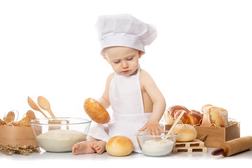 Charming toddler baby in hat of cook and apron sitting on table with bread loaves and cooking ingredients laughing happily Cooking child lifestyle concept
