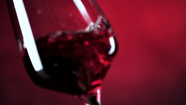 Wein. Rotwein, der in Weinglas &uuml;ber dunklem Hintergrund gie&szlig;t.