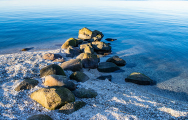 Sunny beautiful seascape with beach, covered with white shells and stone breakwater.  Boulders on the seashore and in the water. 
