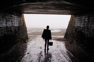 Woman heading out foraging for mussels with her bucket into the misty estuary under the bridge