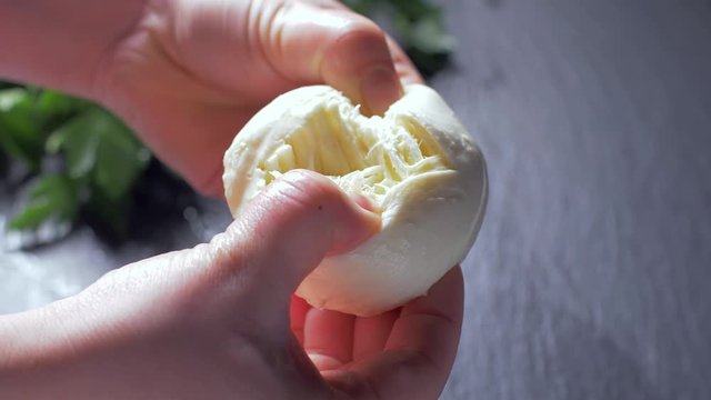 Female hands tear mozzarella cheese. Black background