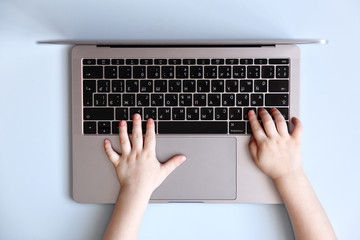 Fototapeta na wymiar Kid hands typing on laptop keyboard on blue background, top view