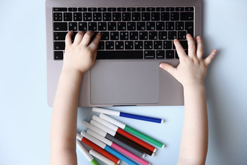 Kid hands typing on laptop keyboard on blue background, top view