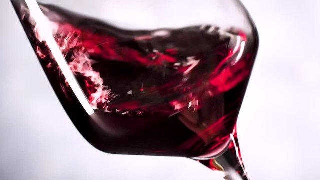 Wein. Rotwein, der in Weinglas &uuml;ber dunklem Hintergrund gie&szlig;t.
