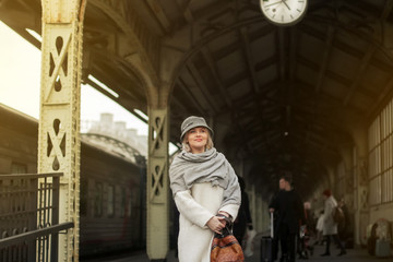 Naklejka na ściany i meble Passengers train go on the platform. Travelling by train. A woman in a white coat and hat stands on the platform. Travel concept.