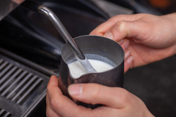 A baristas hands steaming milk for a fat white in a coffee shop