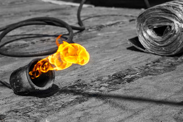 gas burner with fire and roll of roofing material on blurred background with bokeh effect