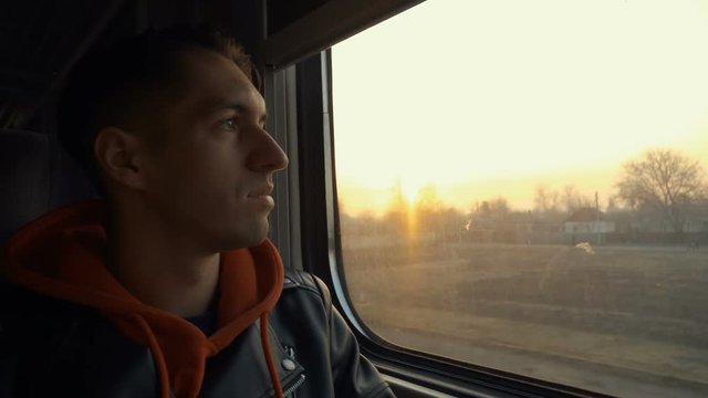 Young man having train journey. Man looking out the window during train ride at sunset